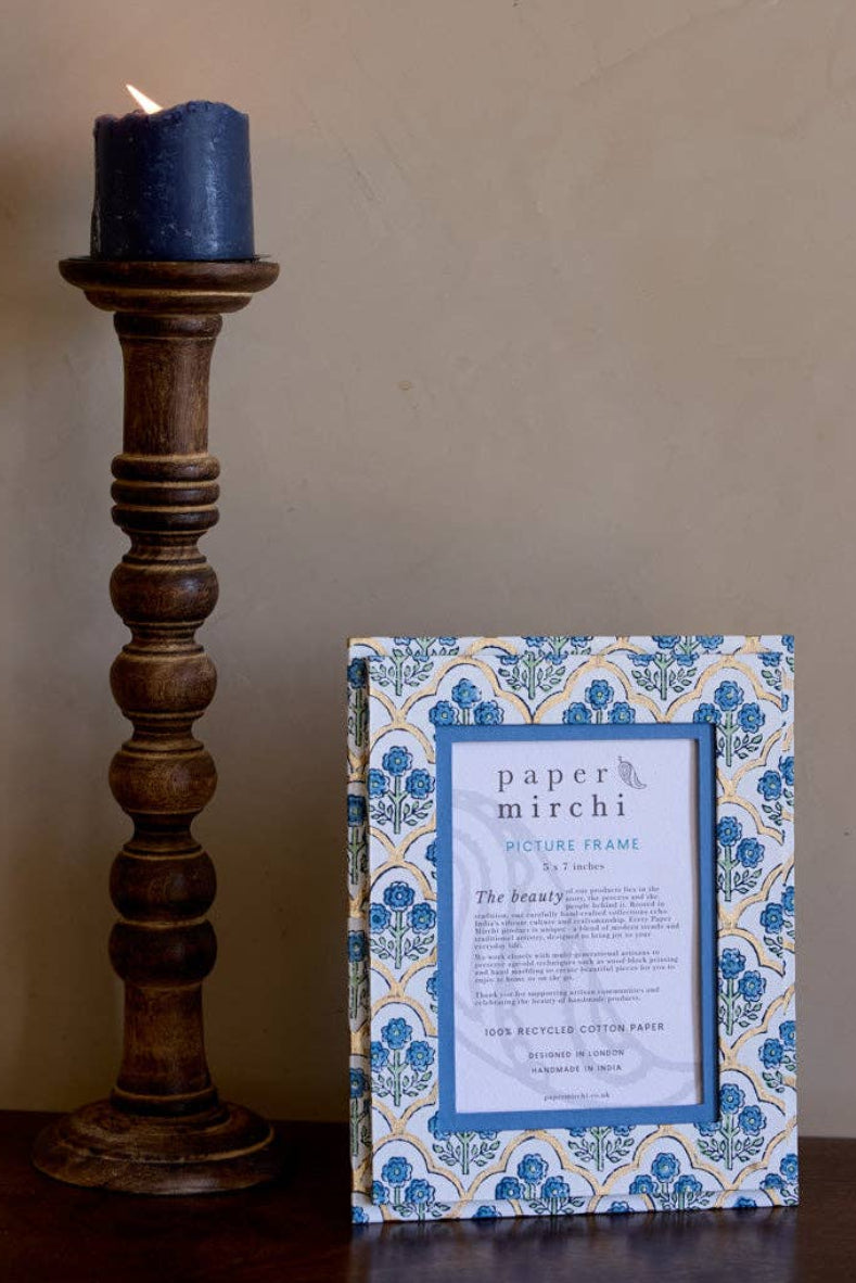 Decorative candle holder with a blue candle and a framed print on a wooden surface.