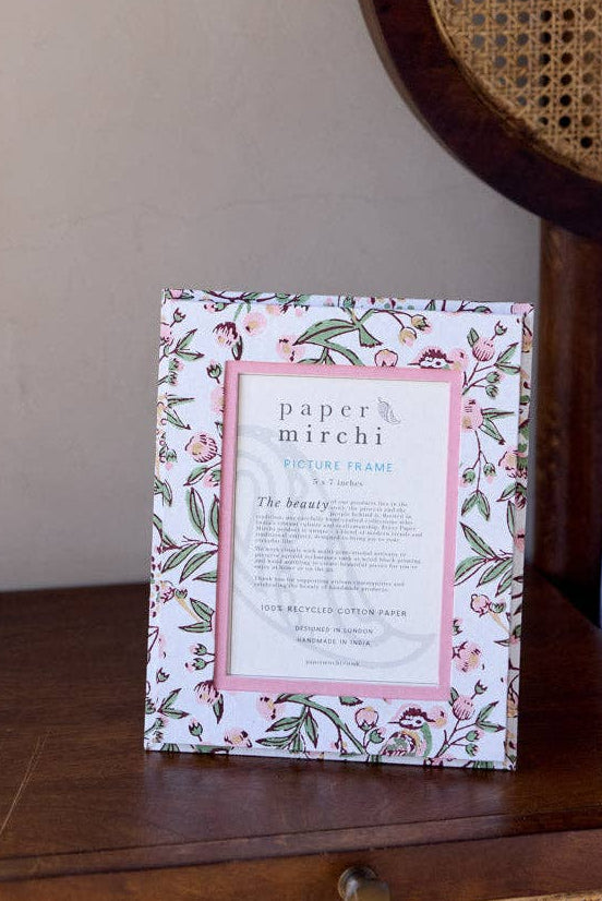 Framed floral print on a wooden nightstand next to a bed with a wicker headboard.
