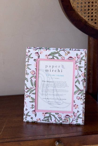 Framed floral print on a wooden nightstand next to a bed with a wicker headboard.