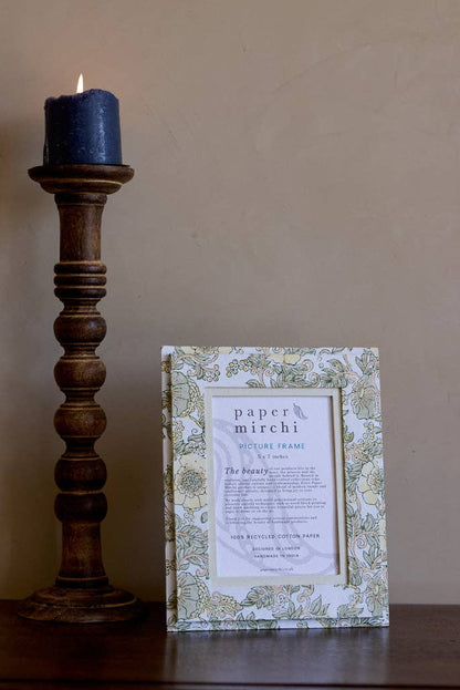 Wooden candlestick with a lit candle and a framed print on a wooden surface against a beige wall.