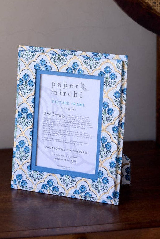 Decorative frame with a blue and white pattern on a wooden nightstand next to a bed with a wicker headboard.